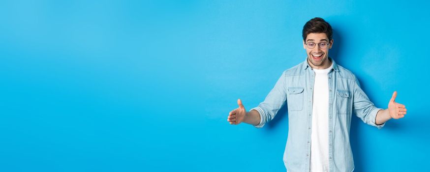Excited handsome man showing big size object and looking amazed, standing over blue background.