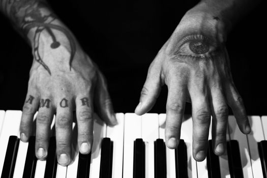 Tattooed mans hands on the keyboard of a piano. Dark background