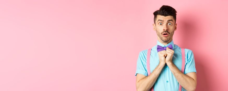 Startled and worried classy man in moustache, gasping and holding breath shocked, standing oin bow-tie over pink background.