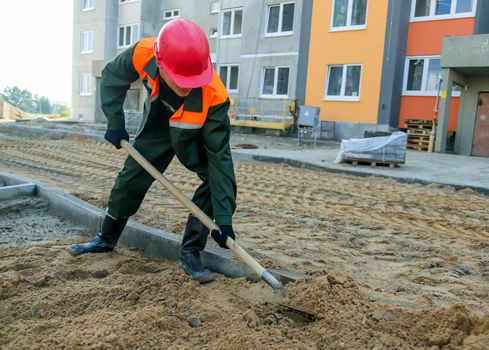 A builder digs sand near the construction site of a residential building.