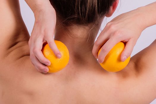 Slim woman is holding orange. Perfect female back without any cellulite.