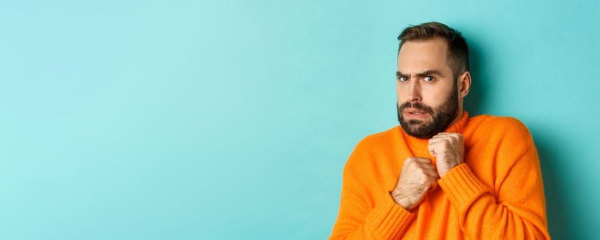 Close-up of scared bearded man looking startled and displeased, jumping from fear, standing over light blue background.