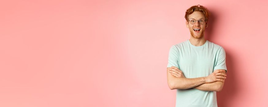 Portrait of cheerful european man in glasses looking amazed at camera, see interesting promotion, standing amused over pink background.