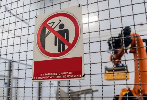 An industrial robotic arm for holding a box in a fence with the inscription: it is forbidden to approach the equipment with rotational movements.