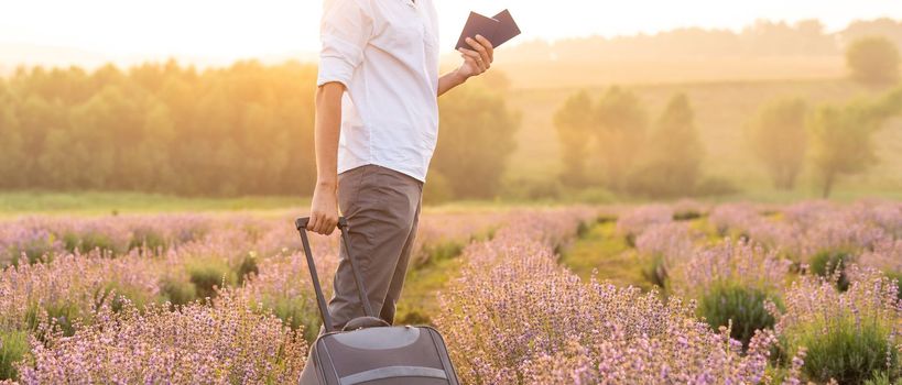 Travel the world. Handsome male passenger holding out his passport smiling cheerfully to the camera in the lavender field.