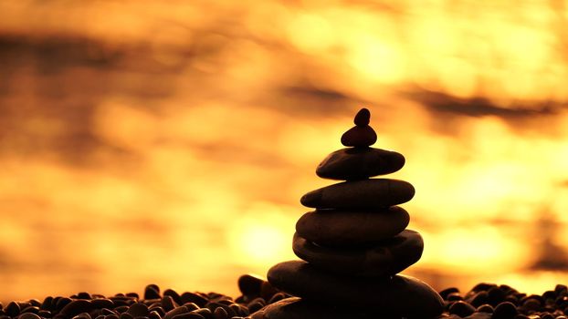 Balanced rock pyramid on pebbles beach. Golden sea bokeh on background. Selective focus, zen stones on sea beach, meditation, spa, harmony, calm, balance concept