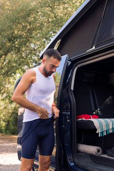 young man dressing up with cycling clothes next to his camper van to go training with his mountain bike, concept of freedom and sport in nature