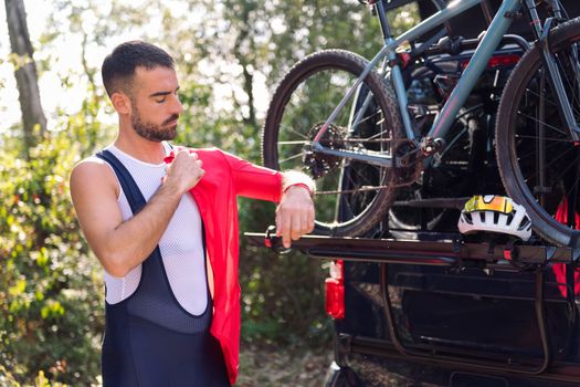young man dressing up with cycling clothes next to his van to go training with his mountain bike, concept of freedom and sport in nature
