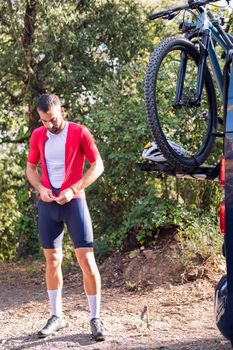 young man dressing up with cycling clothes next to his van to go training with his mountain bike, concept of freedom and sport in nature