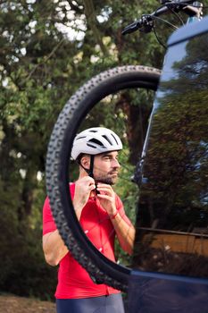 young man putting on cycling helmet next to his van to go training with his mountain bike, concept of freedom and sport in nature
