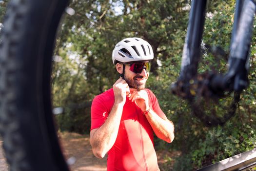 smiling young man putting on cycling helmet next to his van to go training with his mountain bike, concept of freedom and sport in nature