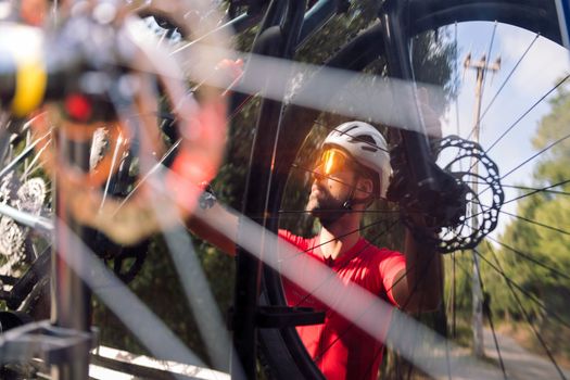 reflection in the rear window of a van of a young man wearing a helmet and cycling goggles taking his mountain bike off the bike rack for a training ride, concept of freedom and sport in nature