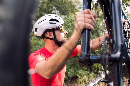 young man in helmet and cycling clothes taking his mountain bike off the bike rack of his van to go for a training ride, concept of freedom and sport in nature