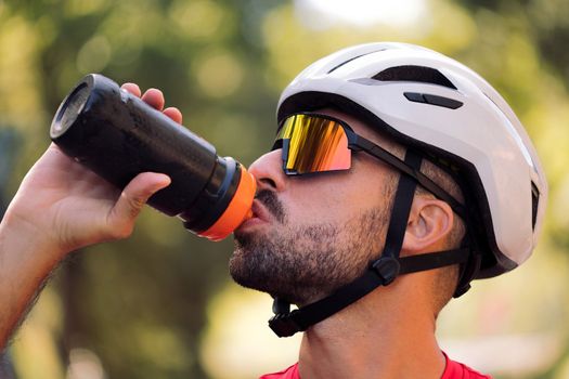 young cyclist with helmet and cycling goggles drinking water from his bottle, concept of freedom and sport in nature