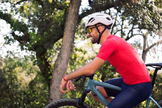 young cyclist smiling happy as he rests sitting on his mountain bike after training, concept of freedom and sport in nature, copy space for text
