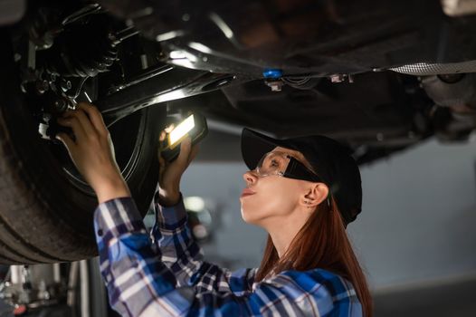 A female mechanic inspects a lifted car. A girl at a man's work