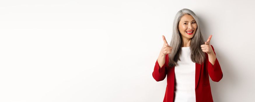 Professional female employer in trendy red blazer and makeup, pointing fingers at camera and smiling, praising something, need you, standing over white background.