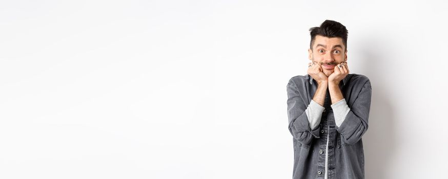 Cute young man with moustache smiling and looking dreamy at camera, gazing at something beautiful, admire true beauty, standing on white background.