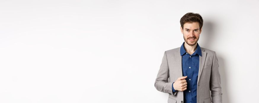 Confident businessman in suit smiling at camera, standing self-assured against white background.