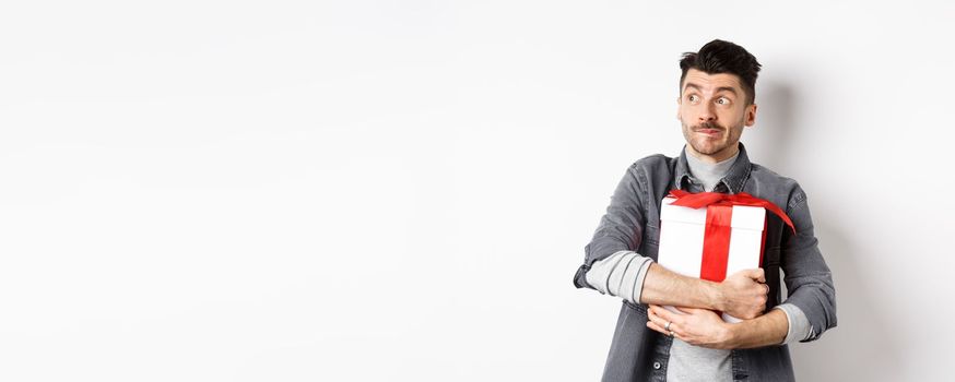 Excited man hugging romantic gift for girlfriend, waiting for valentines date with lover, looking at empty space logo with happy face, standing on white background.