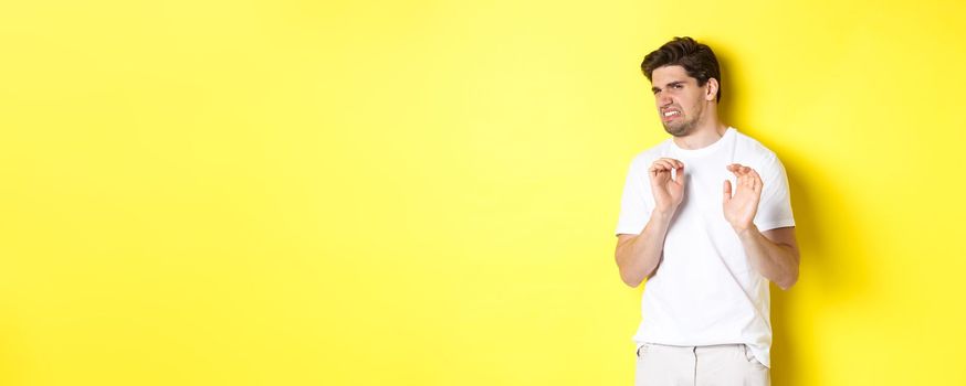Digusted guy refusing and grimacing, looking at something with aversion, standing over yellow background. Copy space