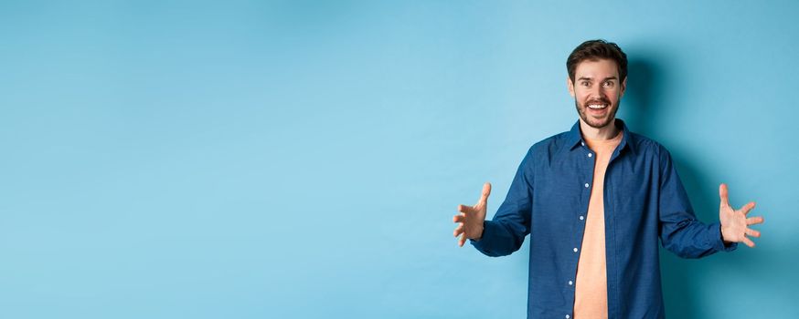 Happy smiling man showing big size object, shaping large thing and looking amazed, standing on blue background.