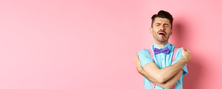 Crying guy hugging himself, feeling sad and lonely, standing unhappy on pink background. Copy space