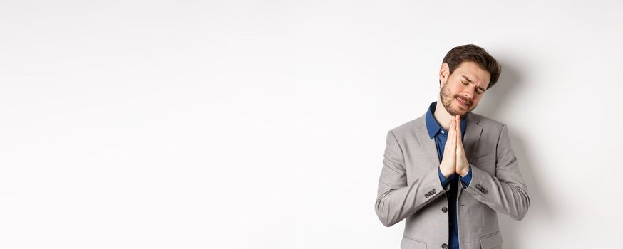 Pleading businessman begging for help, holding hands in pray and asking for favour, need something, say please, standing on white background.