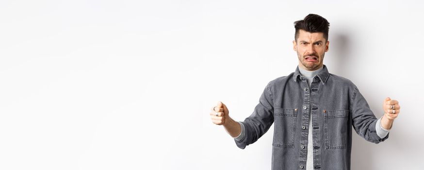 Disgusted guy showing big size object and grimacing from dislike and aversion, talking about disgusting large thing, standing on white background.