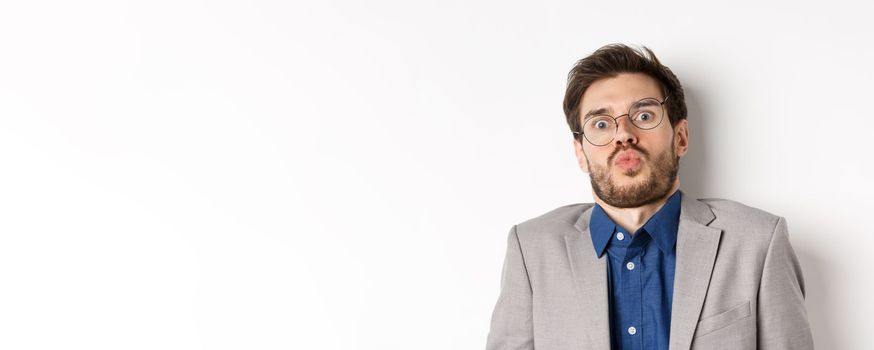 Startled guy in glasses and suit, tilt back and looking shocked or scared at camera, standing against white background.