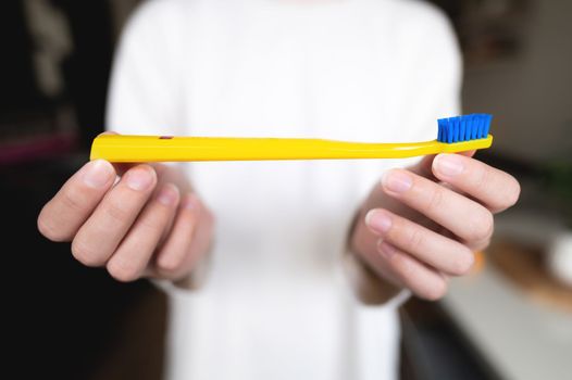 A woman holds a bright toothbrush with two hands against the background of herself in a white sweater, the background is blurred.