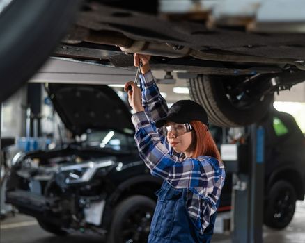 Female mechanic unscrew the nuts on the bottom of the car that is on the lift. A girl at a man's work