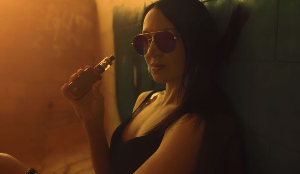 Fashion art portrait of beauty model woman in bright lights with colorful smoke. Smoking girl, Close up of a female inhaling from an electronic cigarette. High quality photo