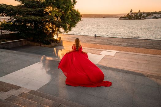 Sunrise red dress. A woman in a long red dress against the backdrop of sunrise, bright golden light of the sun's rays. The concept of femininity, harmony