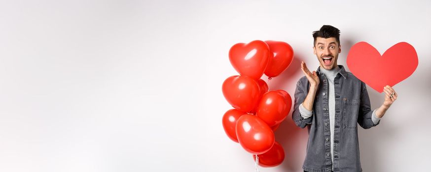 Man scream of joy and happiness, showing big red heart cutout on Valentines day, confess in love, going on romantic date and cheering, standing against white background.