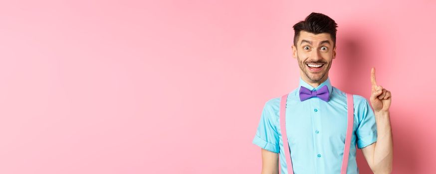 Cheerful caucasian man pitching an idea, raising finger in eureka gesture and smiling, suggesting solution, standing on pink background.