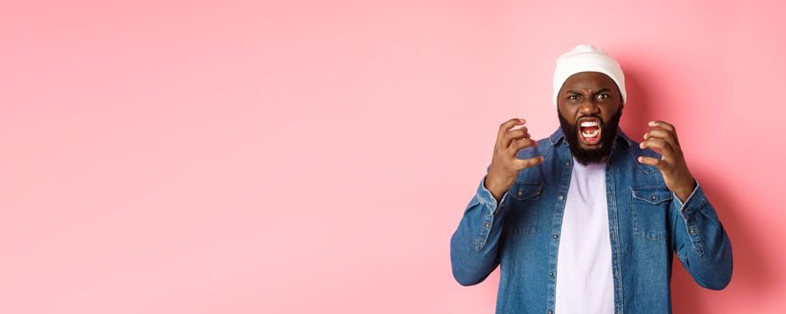 Angry african-american guy shouting and looking pissed-off, scream at camera, standing over pink background.