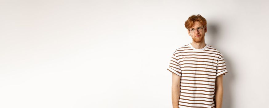 Sad and gloomy redhead man looking upper left corner, sulking and feeling like loser, standing over white background.