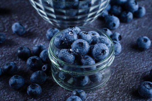 Blueberries organic natural berry with water drops on dark background close-up. Blueberry in glass bowl plate