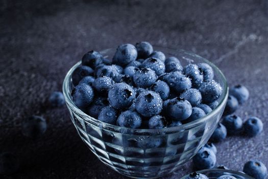 Blueberries organic natural berry with water drops on dark background. Blueberry in glass bowl plate