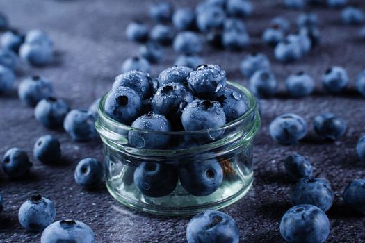 Blueberries with water drops on black background. Blueberry in glass bowl plate