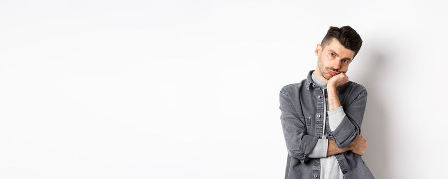 Bored and reluctant stylish guy look at camera without emotions, attend boring meeting, standing on white background.