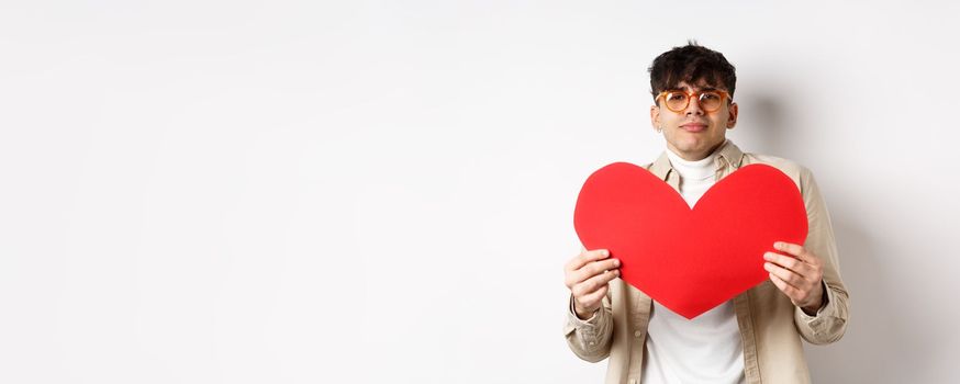 Passionate man waiting for lover with big red heart on Valentines day, looking romantic and with love, standing over white background.