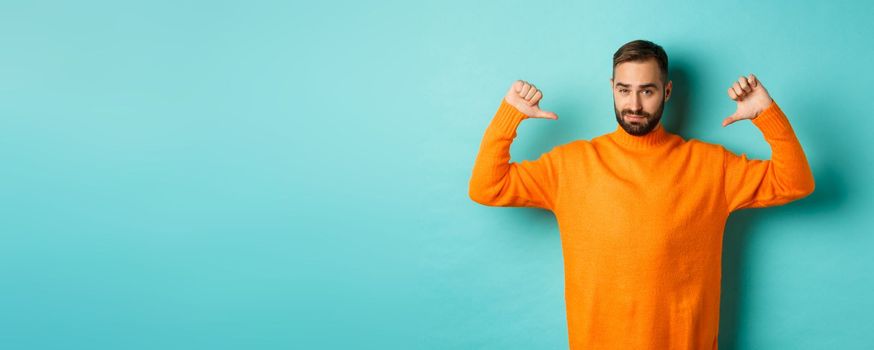 Confident attractive guy pointing at himself, show-off or brag, standing over light blue background.