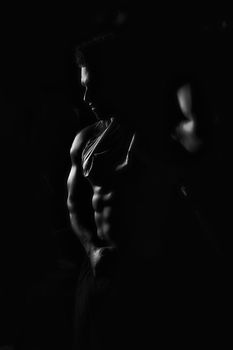 The athlete shows his body and abs, creative photo, black and white photo, contours, muscles stand out, beautiful body, physique, relief, sexy guy, young.