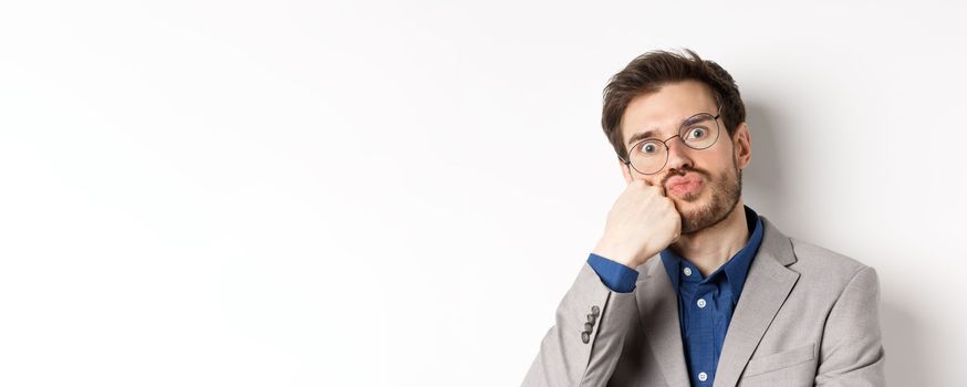 Bored funny office worker in glasses, pouting and holding breath, staring with popped eyes at camera, white background.