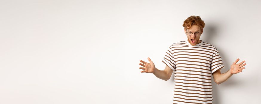 Impressed redhead man in glasses showing length of something big, demonstrate large size and looking amazed, standing over white background.