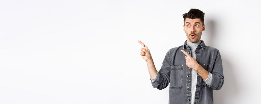 Stylish guy say wow, pointing and looking left with excited face, showing banner logo, standing on white background.