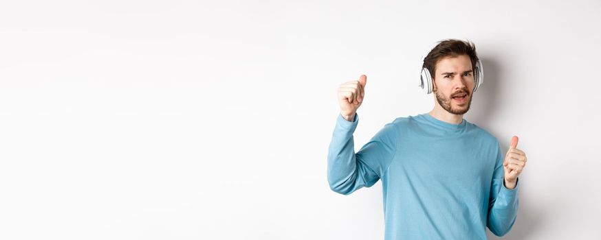 Cheeky guy dancing and having fun in wireless headphones, enjoying good sound quality, white background.