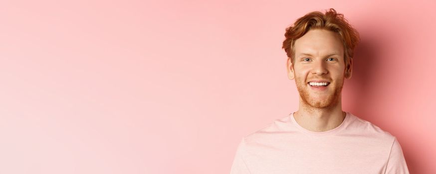 Headshot of happy redhead man with beard and white teeth, smiling excited at camera, standing over pink background.